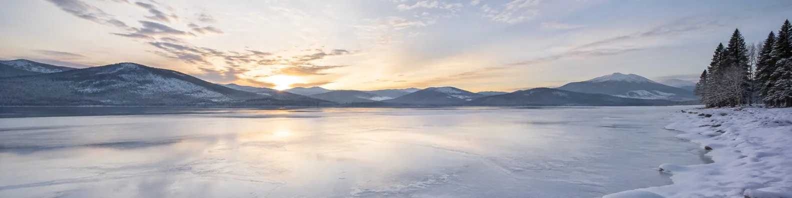 Frozen lake landscape LinkedIn background banner with smooth ice, snowy shoreline, distant mountains, and soft winter sky