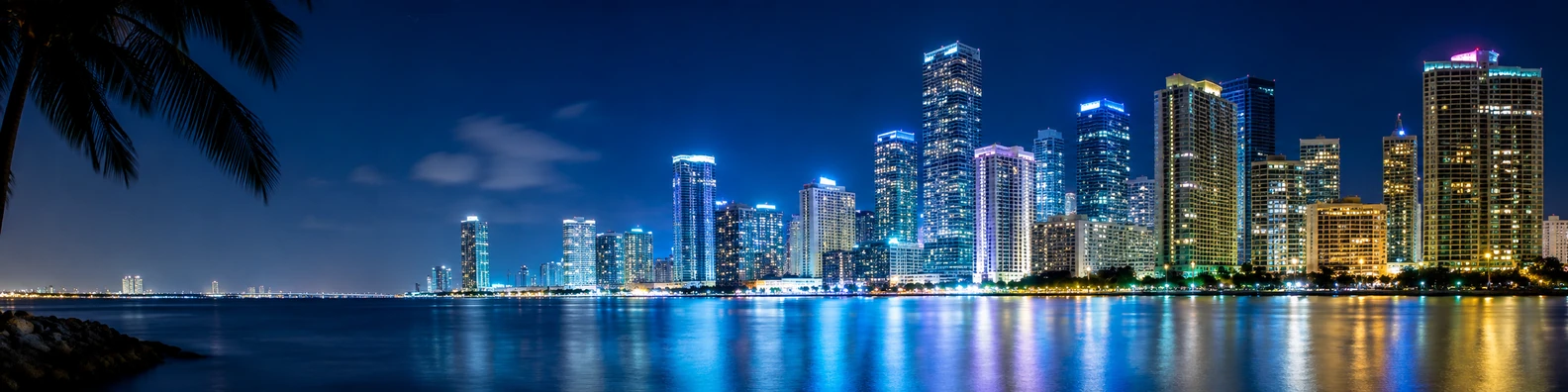 Miami skyline at night with illuminated high-rise buildings and water reflections LinkedIn background banner