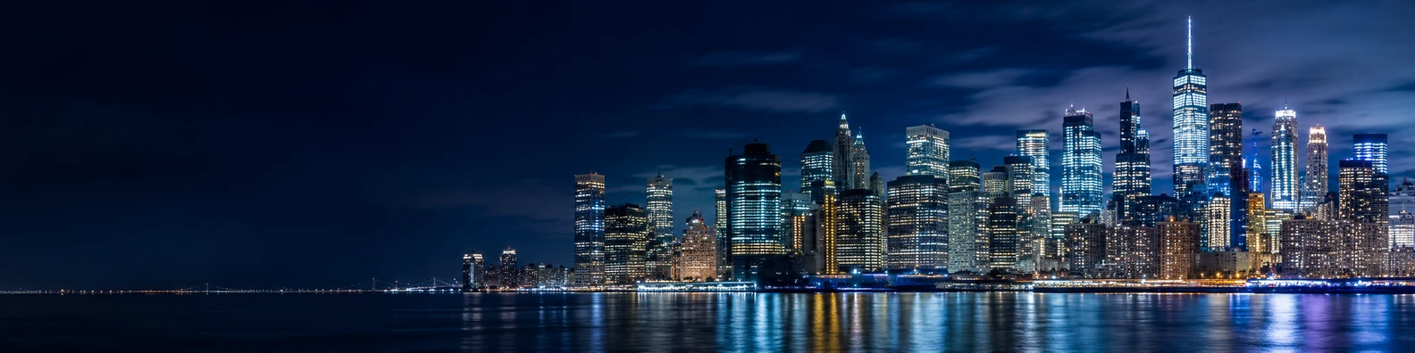 New York City skyline at night with illuminated skyscrapers and calm water reflections LinkedIn background banner