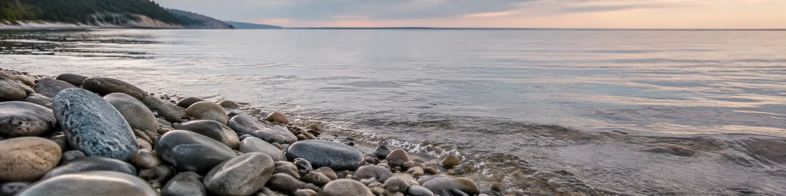 Smooth stones beside a calm shoreline with gentle water LinkedIn background banner